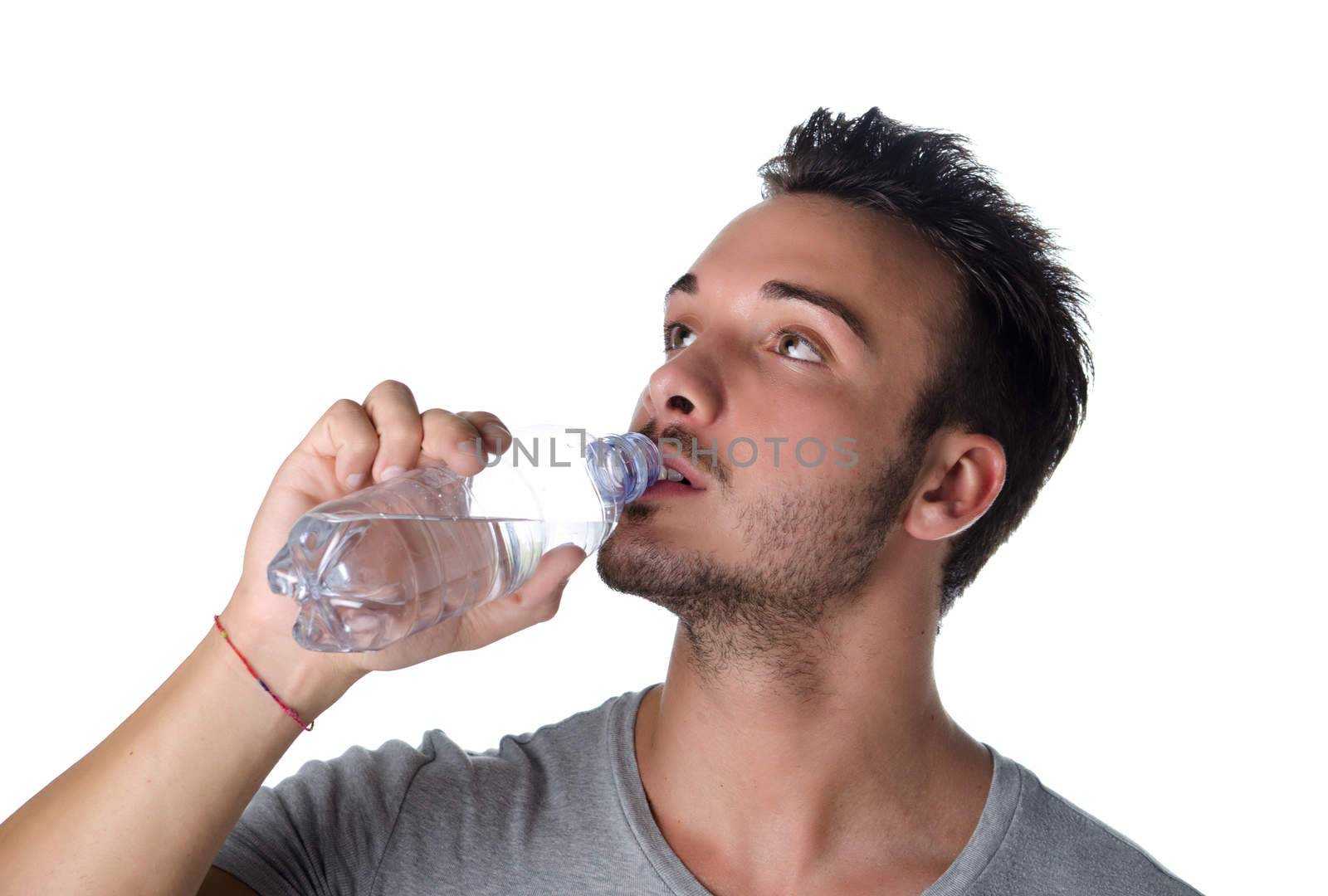 Fit and handsome young man drinking water from plastic bottle, isolated on white