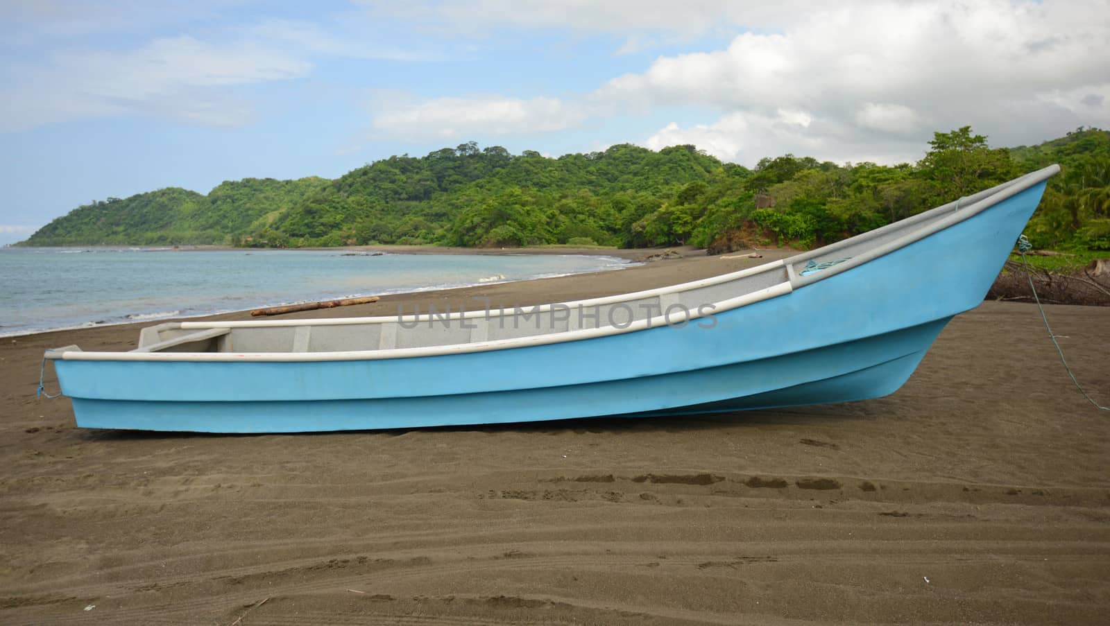 blue boat on beach near ocean will tropical rainforest in background