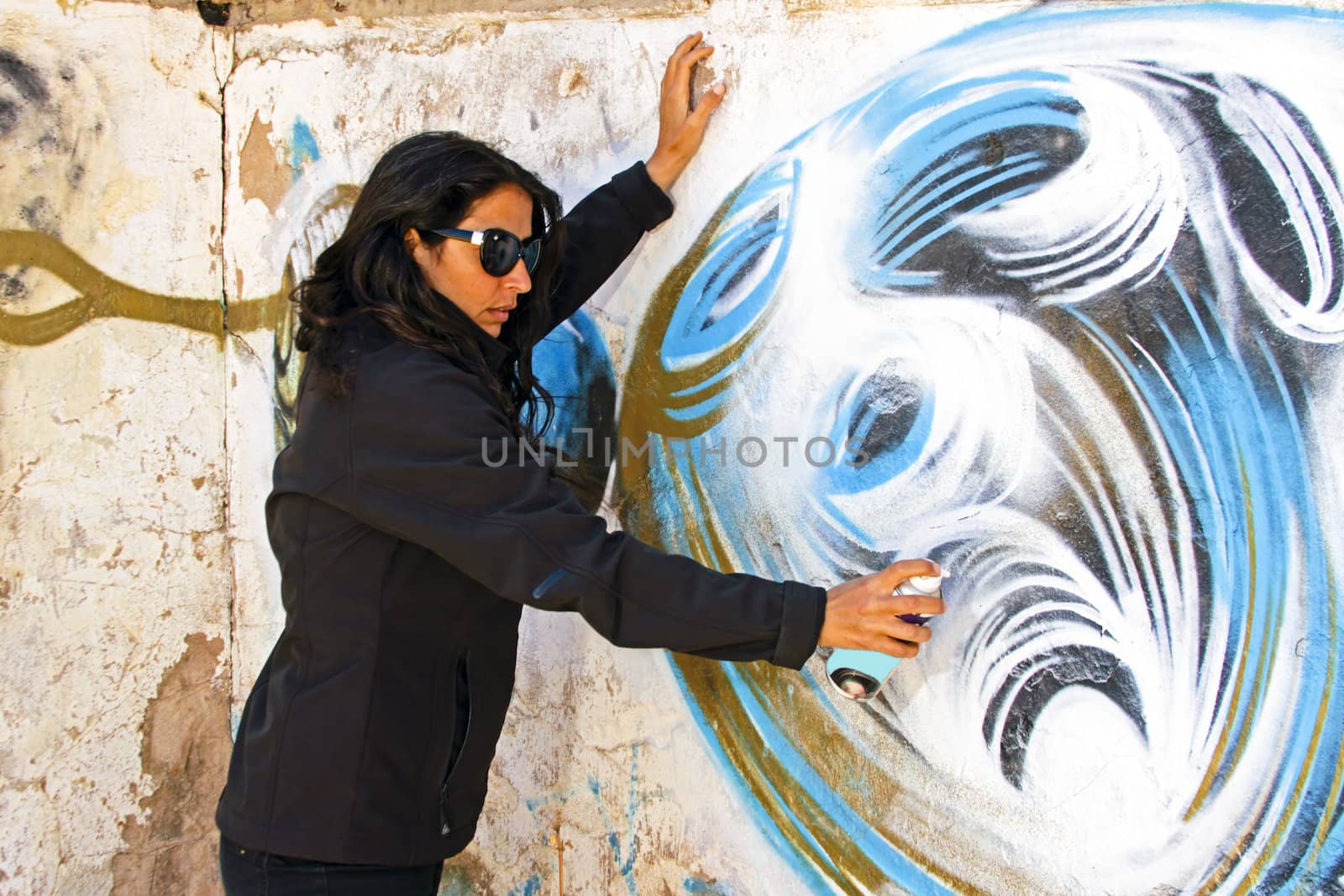 Woman in black spraying at a graffiti brick wall