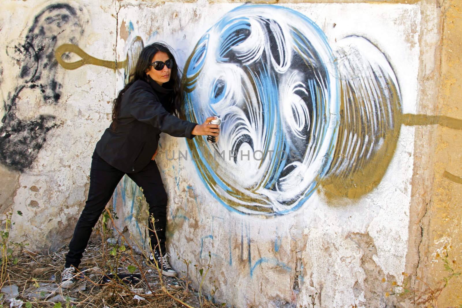 Woman in black spraying at a graffiti brick wall