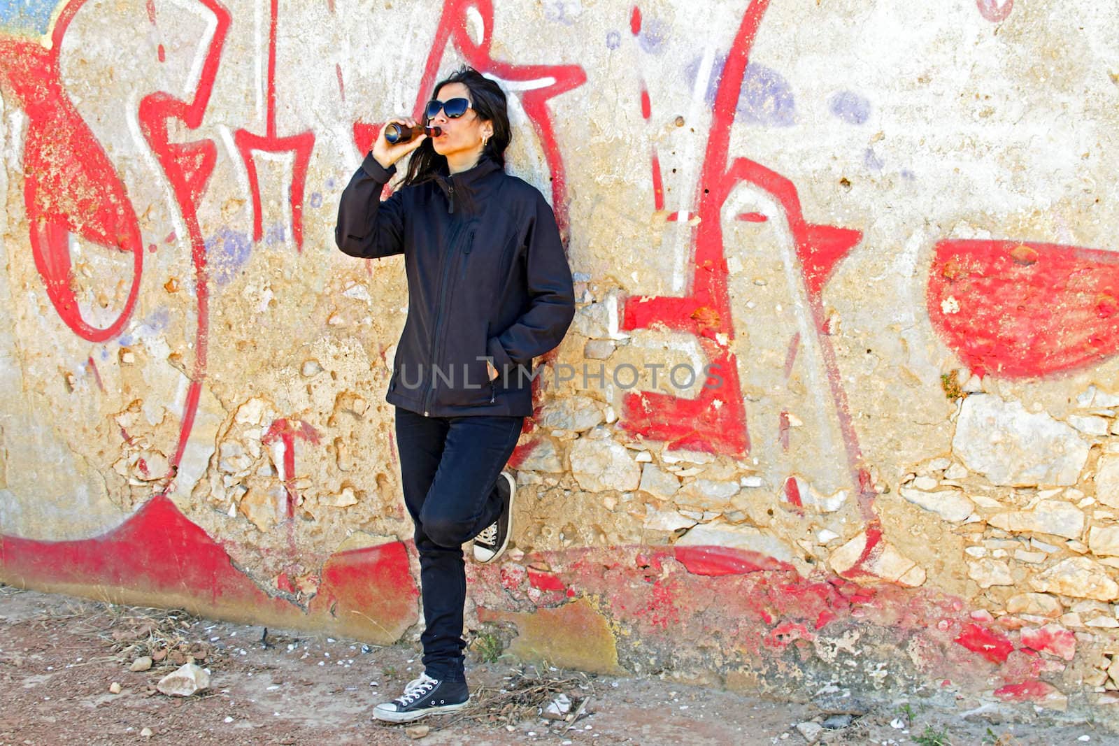 Woman in black drinking beer at a graffiti wall