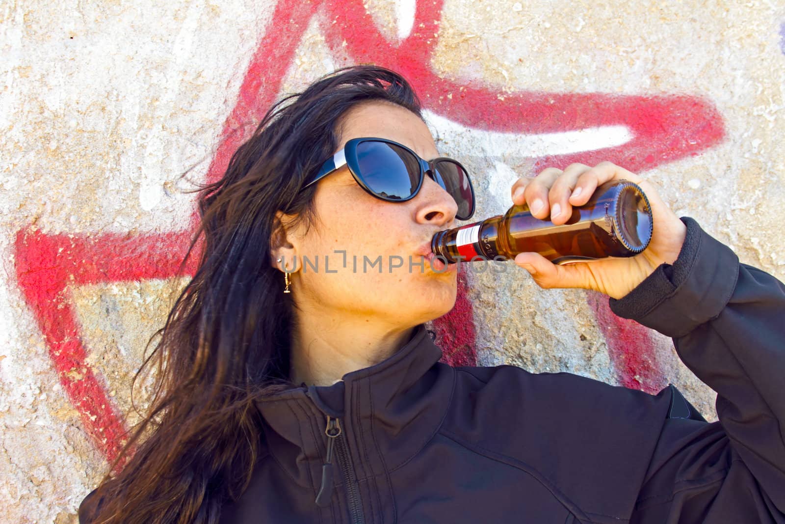Woman drinking beer in front of a graffiti wall