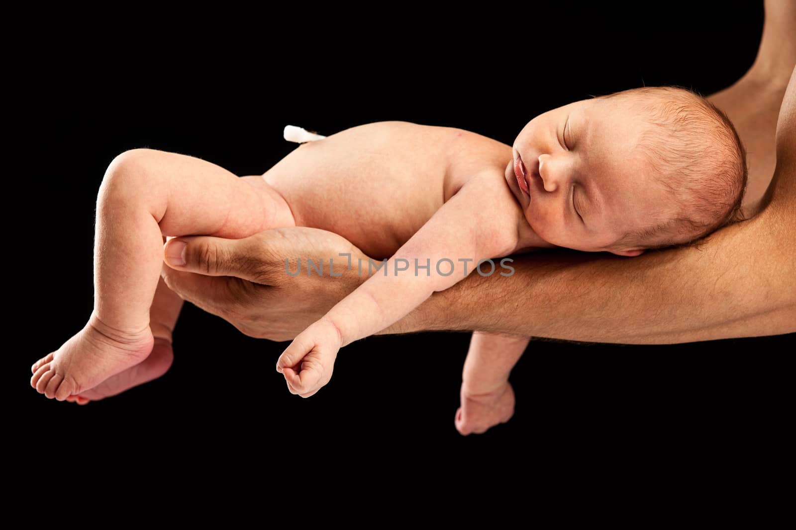 Newborn boy lying on his dad's arms over black background