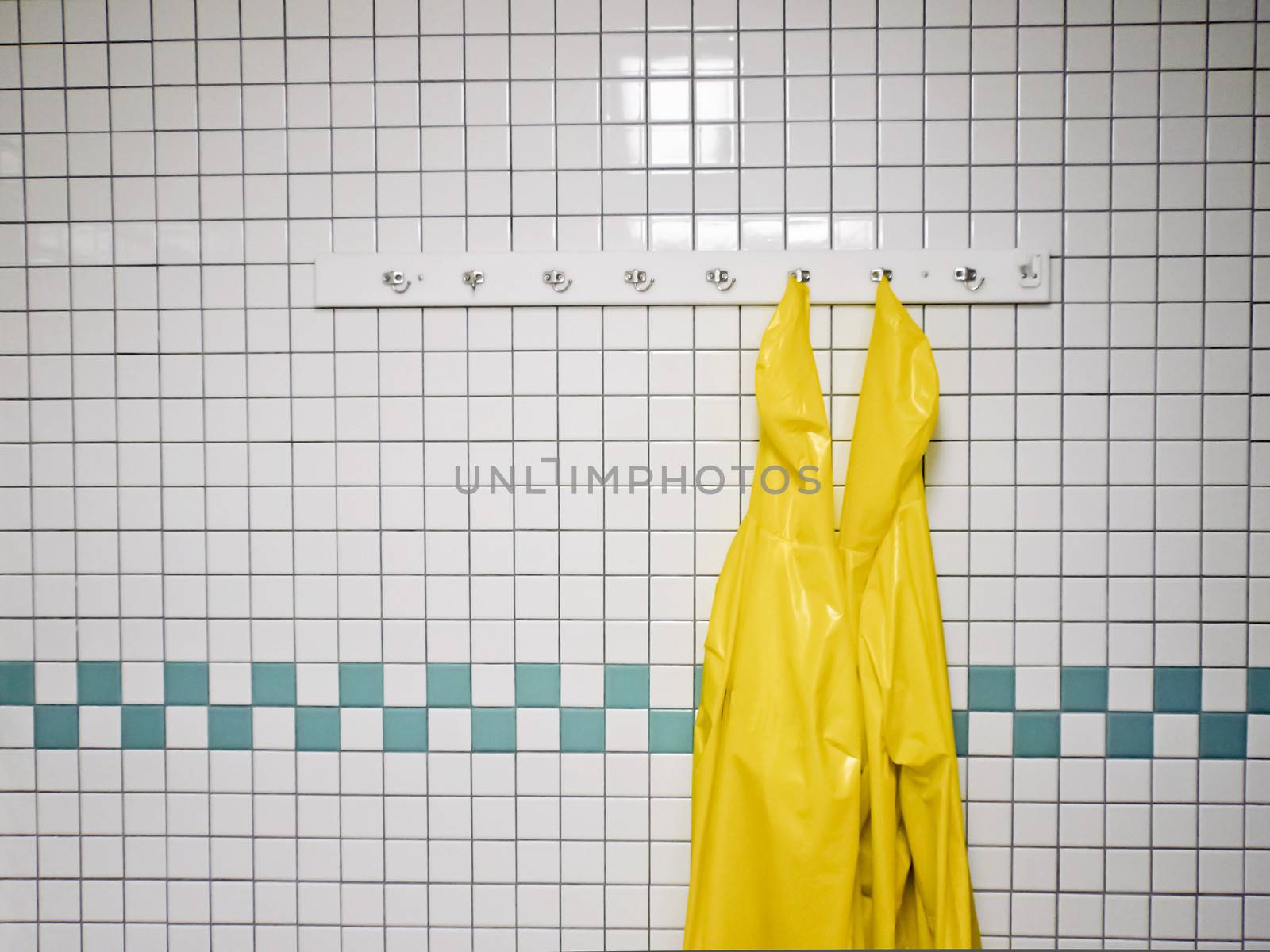Two yellow work aprons hang in a tiled work room.