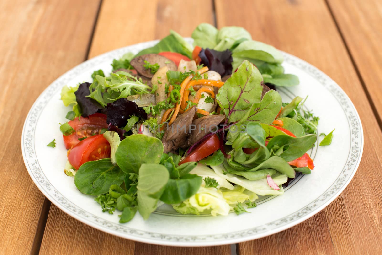 Mixed salad with fried rabbit liver and fresh vegetables on a wooden table.