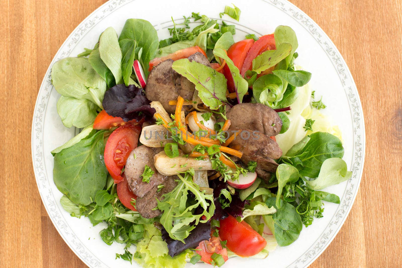 Gourmet salad with fried rabbit liver and fresh vegetables on a wooden table.
