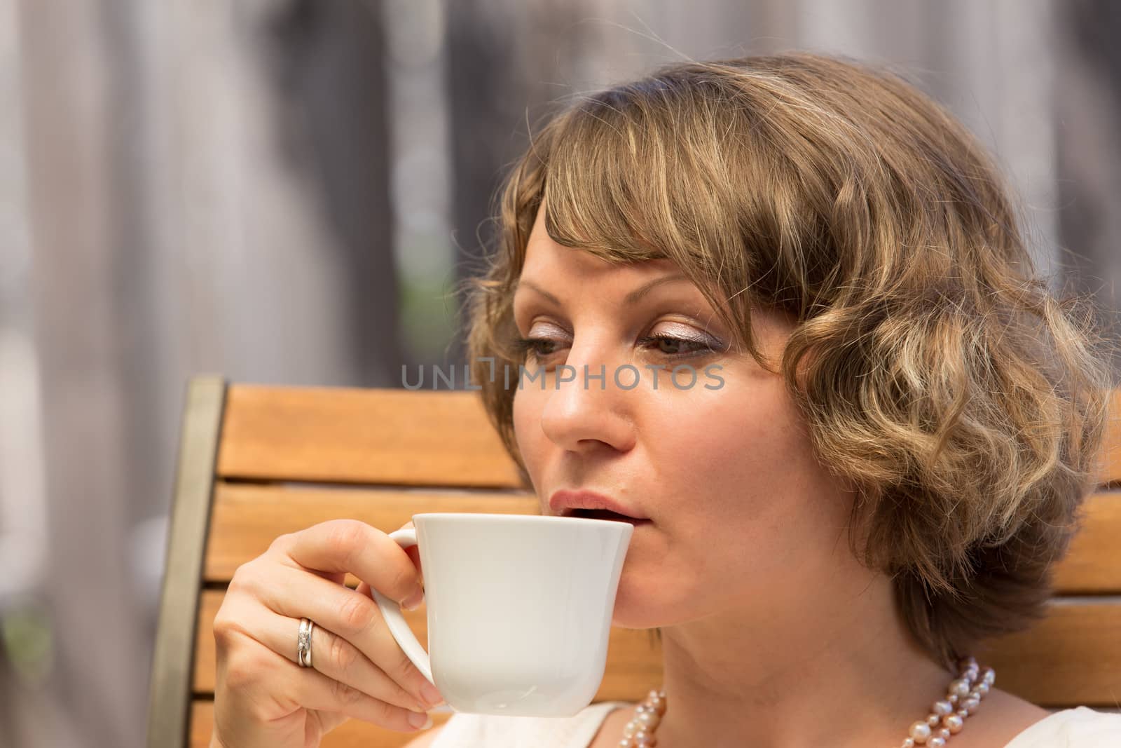 Attractive woman drinking a cup of coffee on wooden chair.