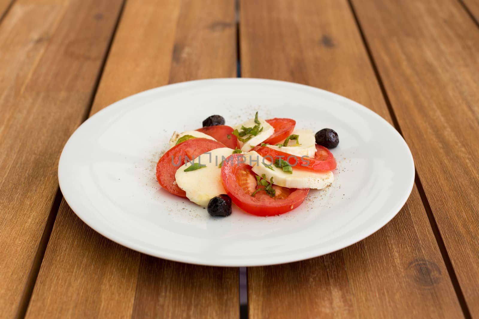 Fresh mozzarella, tomatoes salad in white plate on a wooden table.
