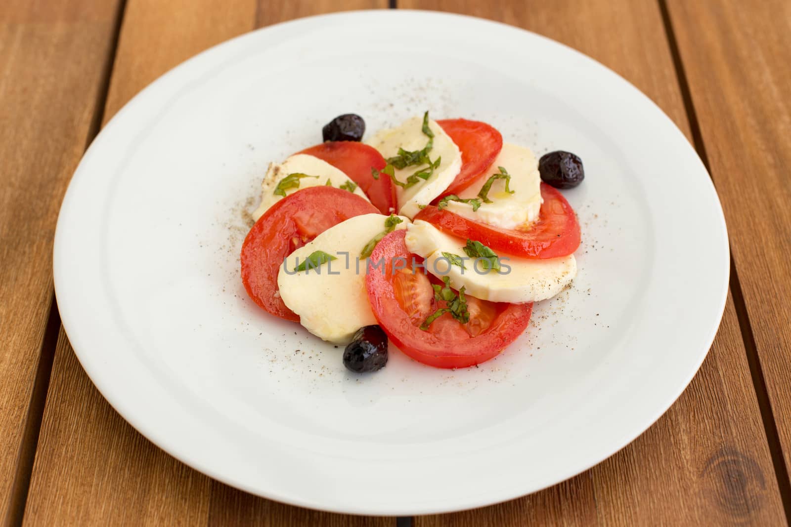 Delicious mozzarella, tomatoes salad in white plate on a wooden table.