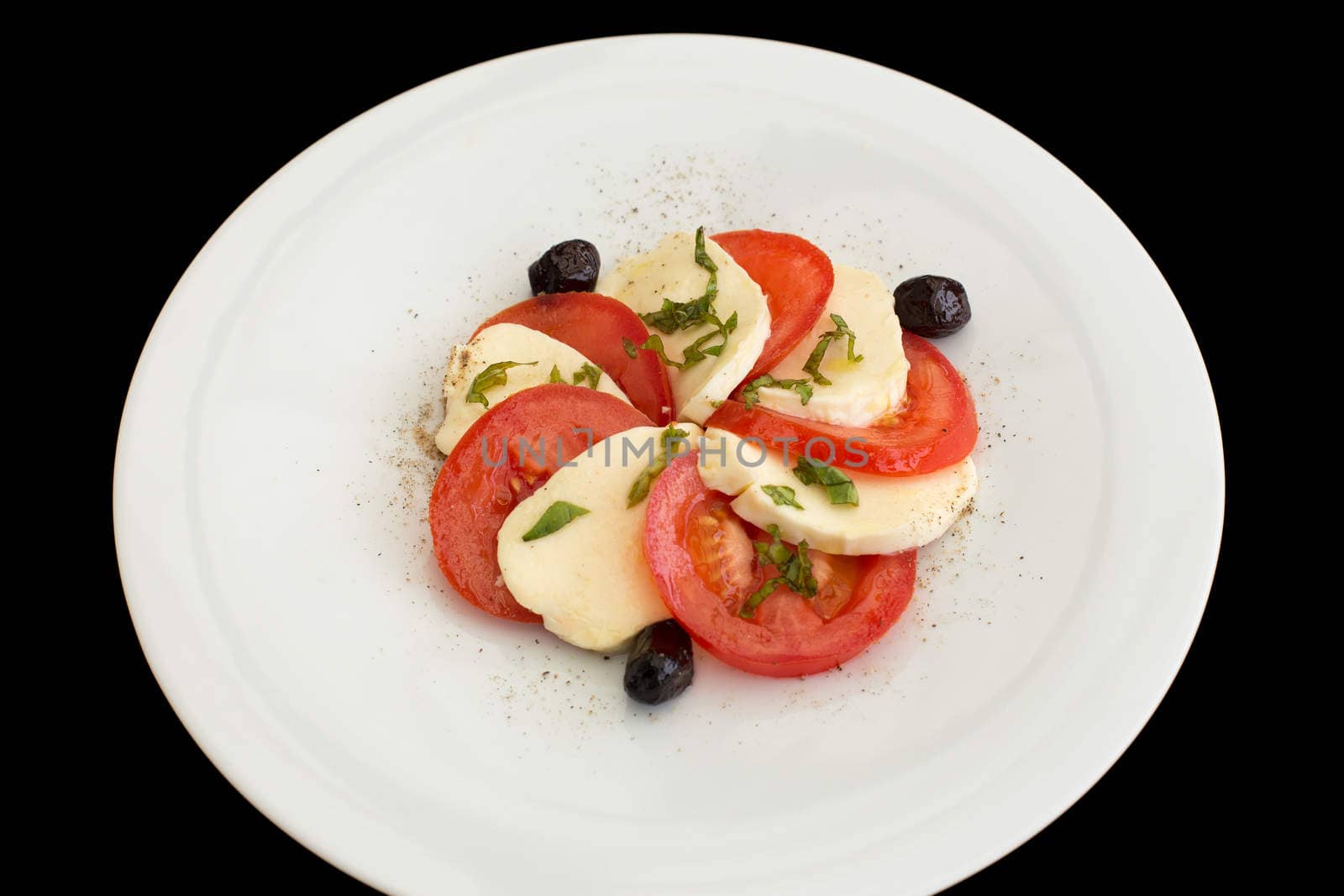 Delicious caprese salad in a white plate on a black background.