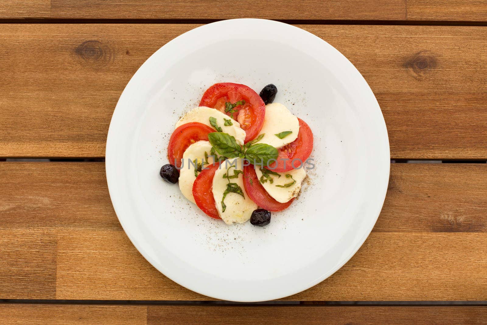 Tomatoes and mozzarella salad in white plate on a wooden table.
