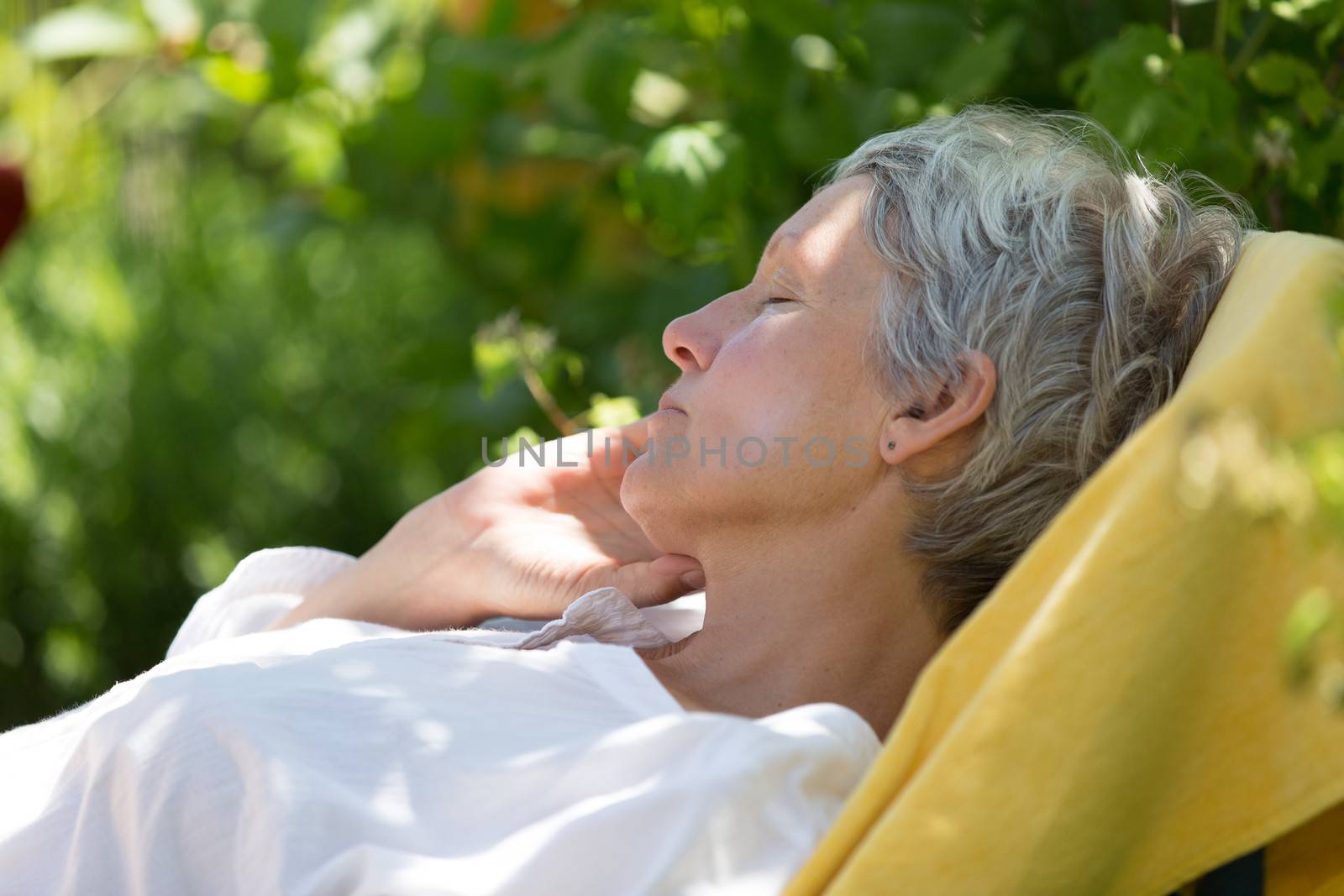 Aged woman with white hairs sleeping on lounger in her garden.
