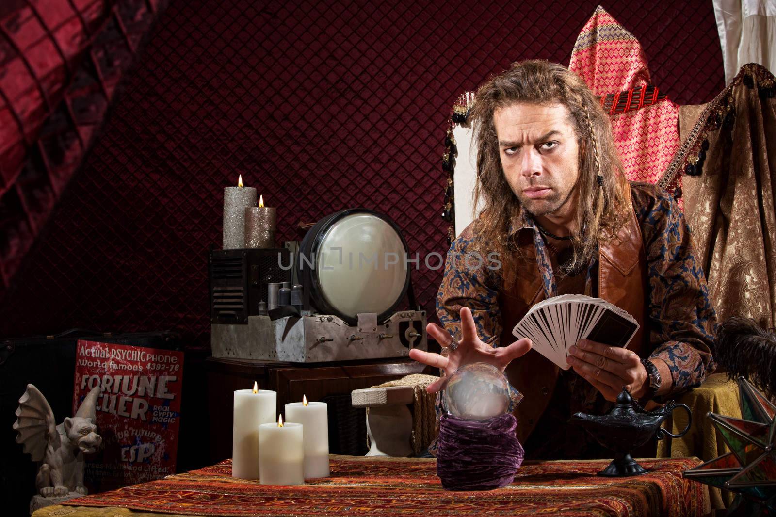 Male fortune teller with tarot cards waving hand over crystal ball