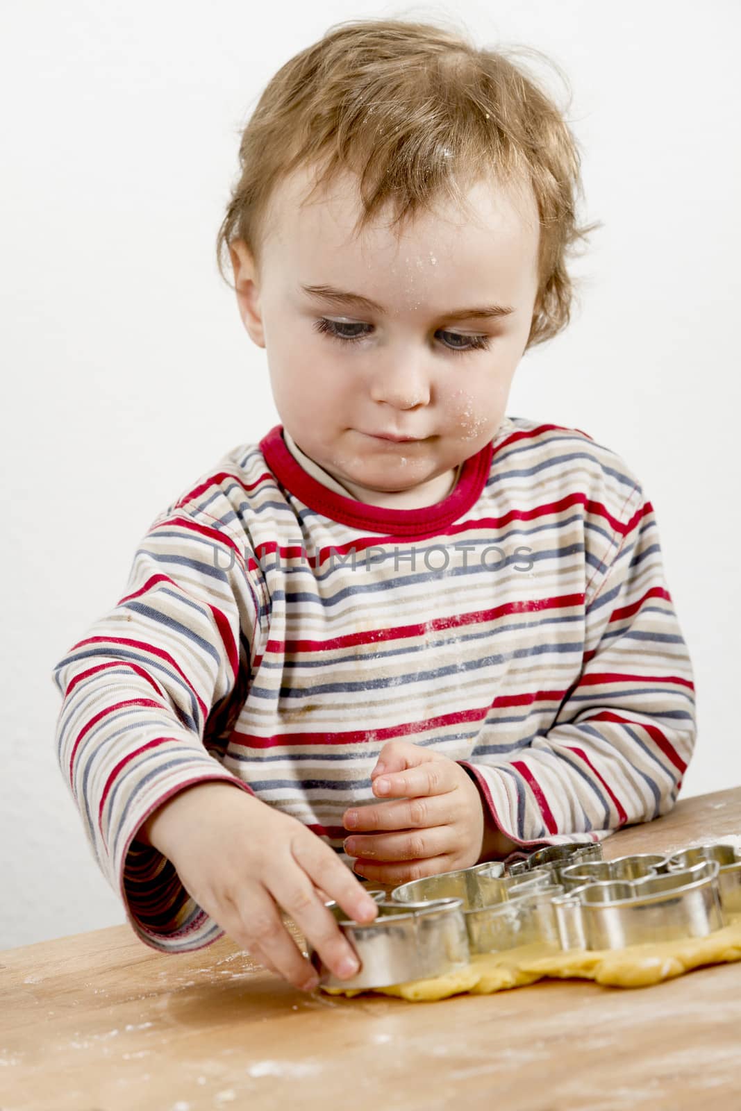 vertical image of 2 year old child making biscuit  at wooden desk