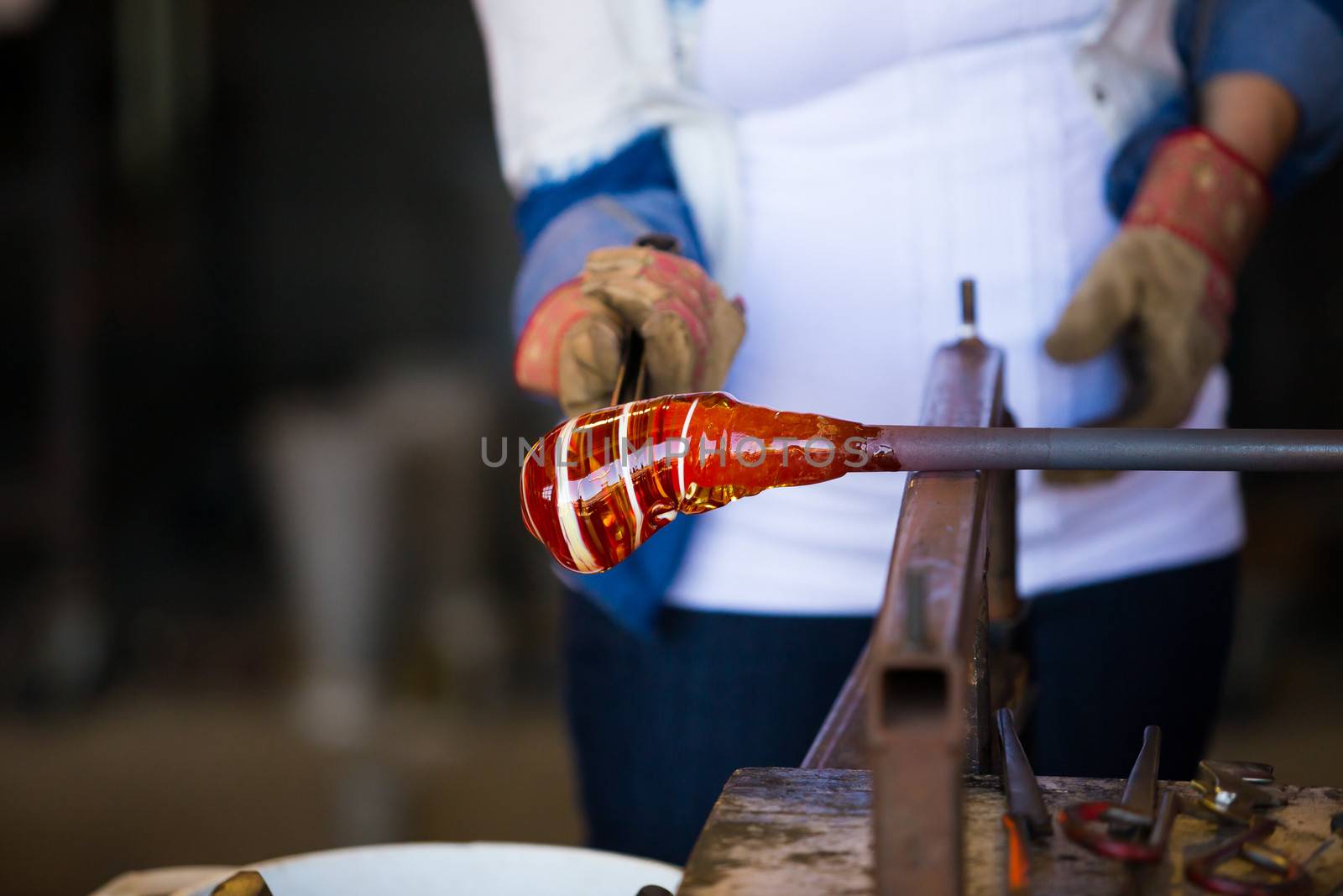 A female is blowing glass and using a wooden shaping tool to form the shape she wants the glass to end up as. The glass is hot and molten so she has to use water with the wood.