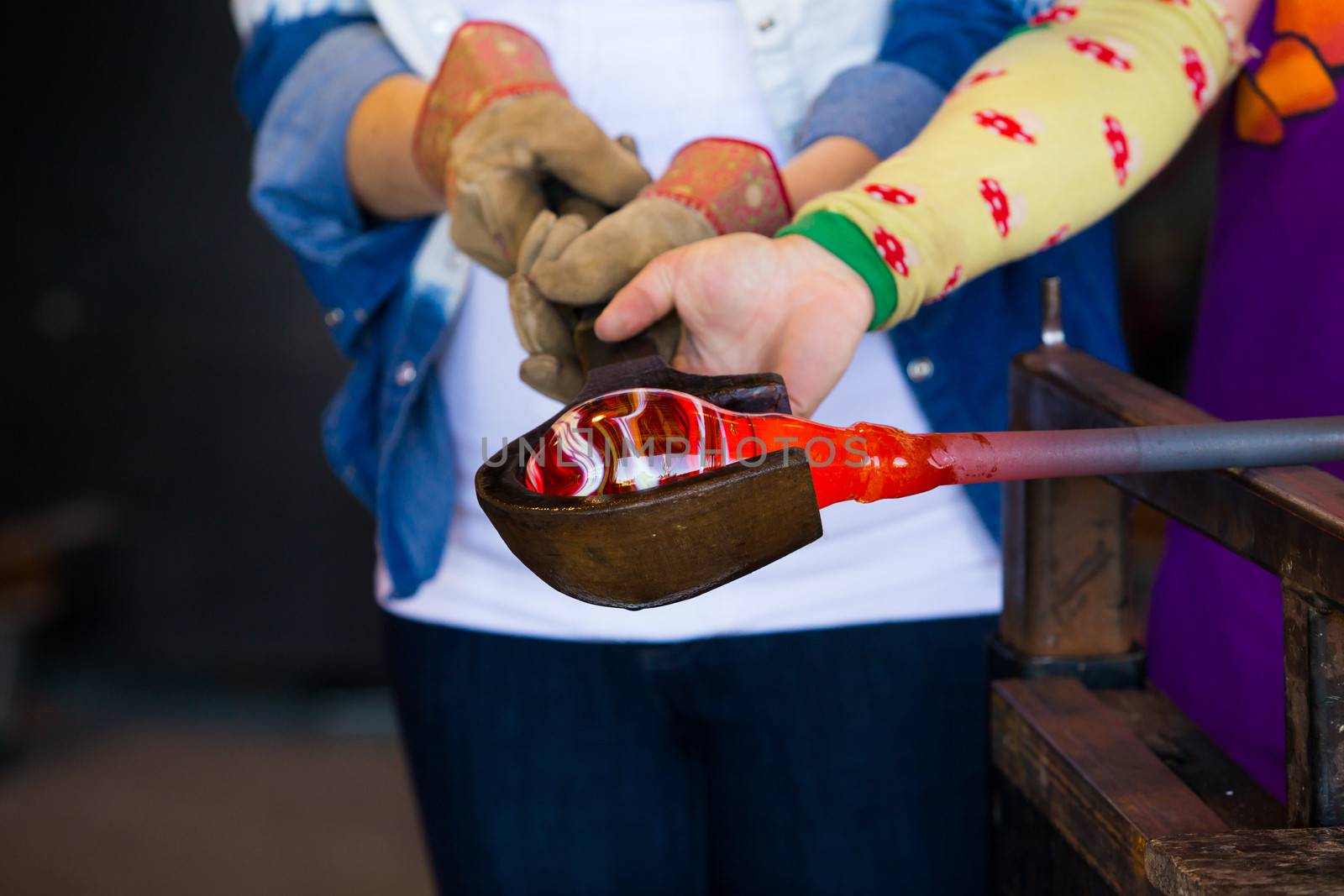 A female is blowing glass and using a wooden shaping tool to form the shape she wants the glass to end up as. The glass is hot and molten so she has to use water with the wood.