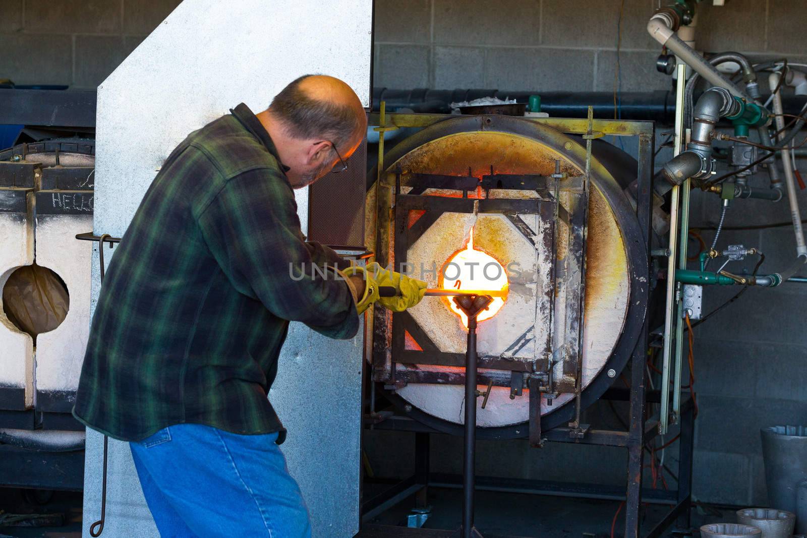 A man fires up his glass while glassblowing using a furnace that is extremely hot.