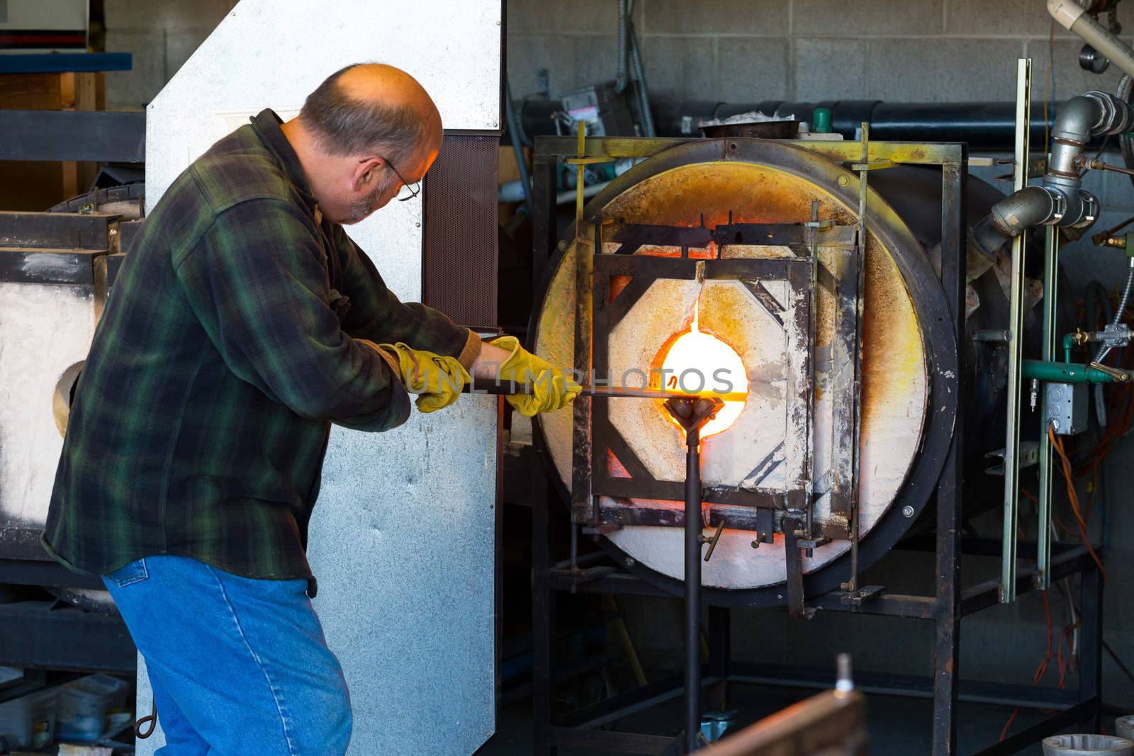 A man fires up his glass while glassblowing using a furnace that is extremely hot.