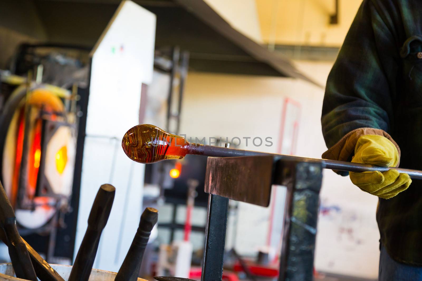 A very talented glassblower is forming and shaping glass in a studio for glass making. He is creating a fluted bowl from this piece of molten glass.