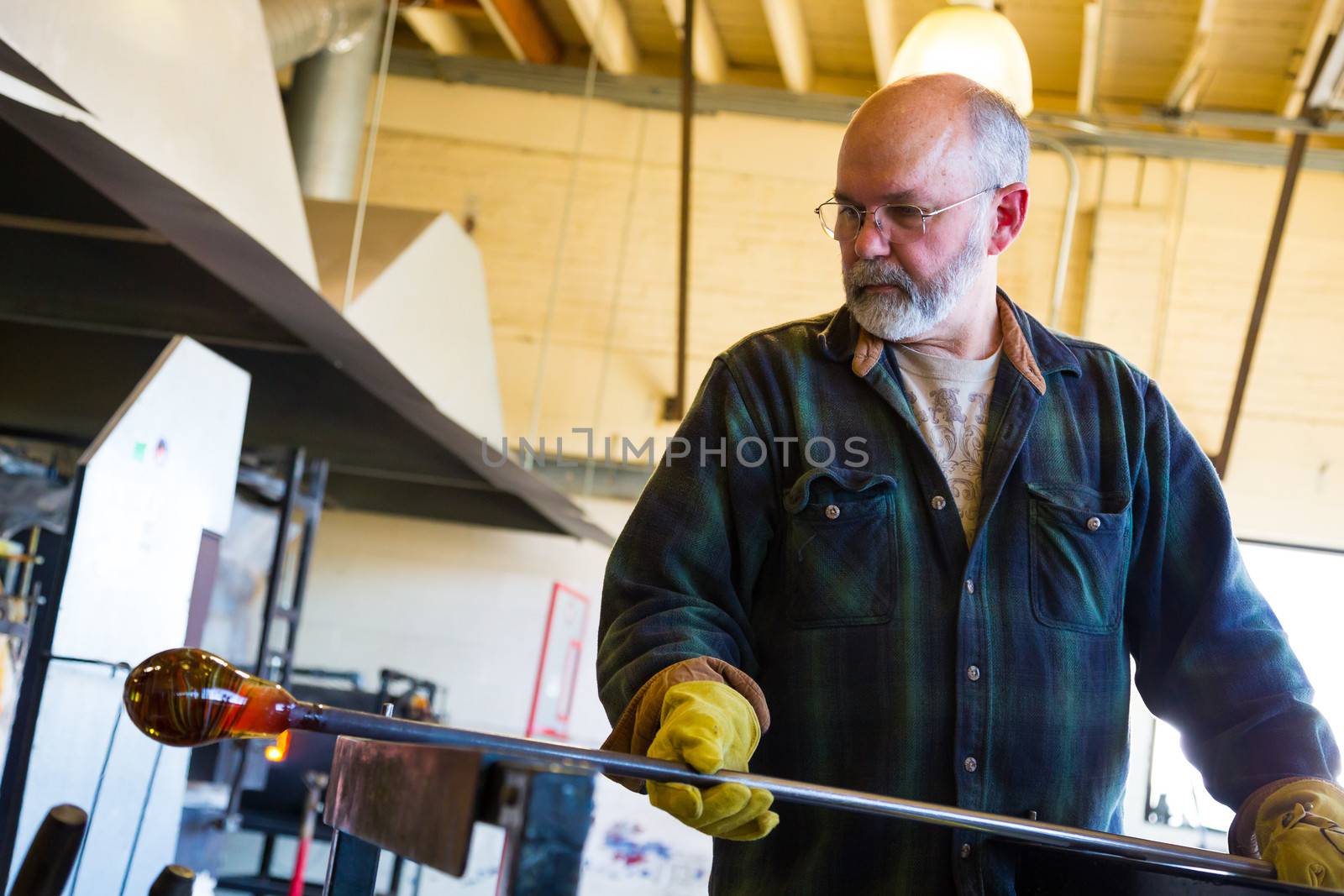 A very talented glassblower is forming and shaping glass in a studio for glass making. He is creating a fluted bowl from this piece of molten glass.