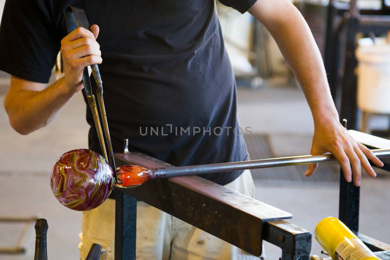 A man takes motlen glass and shapes it using some specialized tools for glassblowing art.