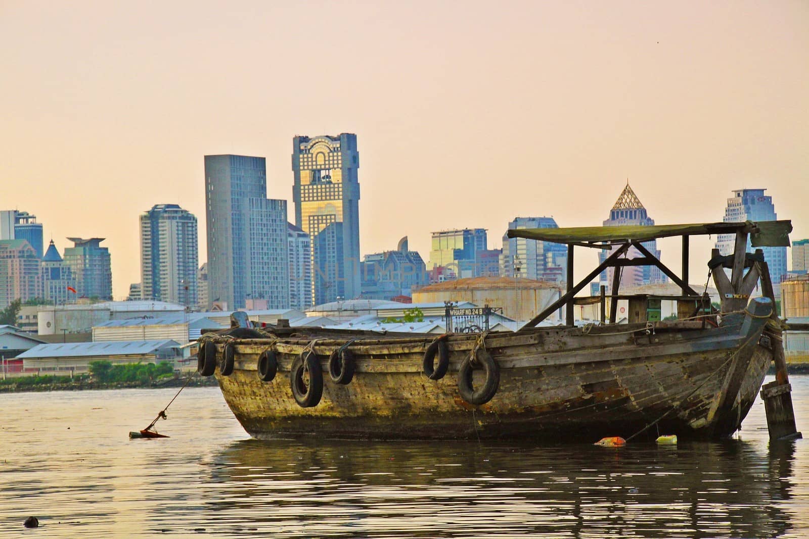 Old disfunctioned boat at sunset on the Chao Phraya river in the outskirts of Bangkok, Tahiland with panorama of Silom district