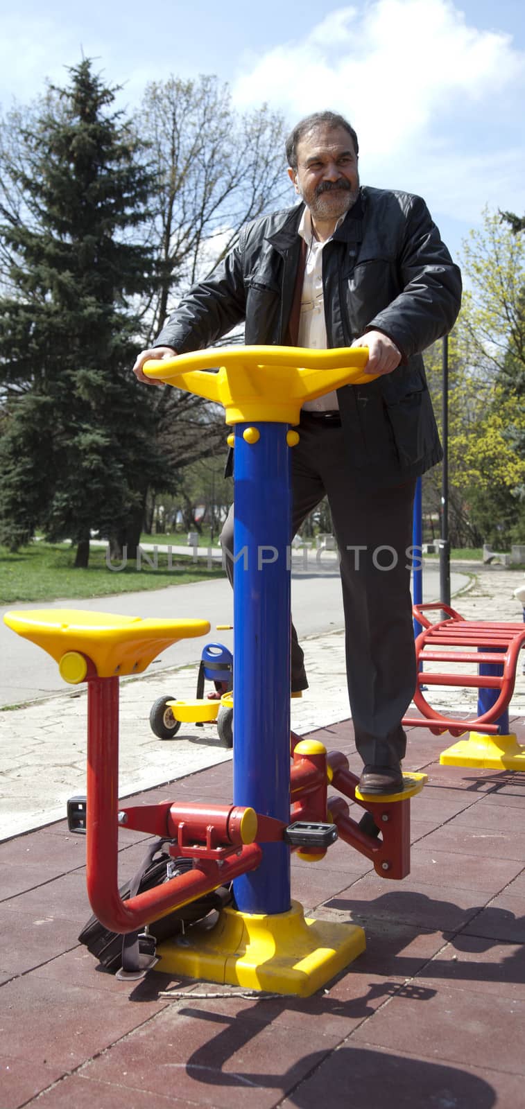 Adult man exercising on colourful fitness machine in park