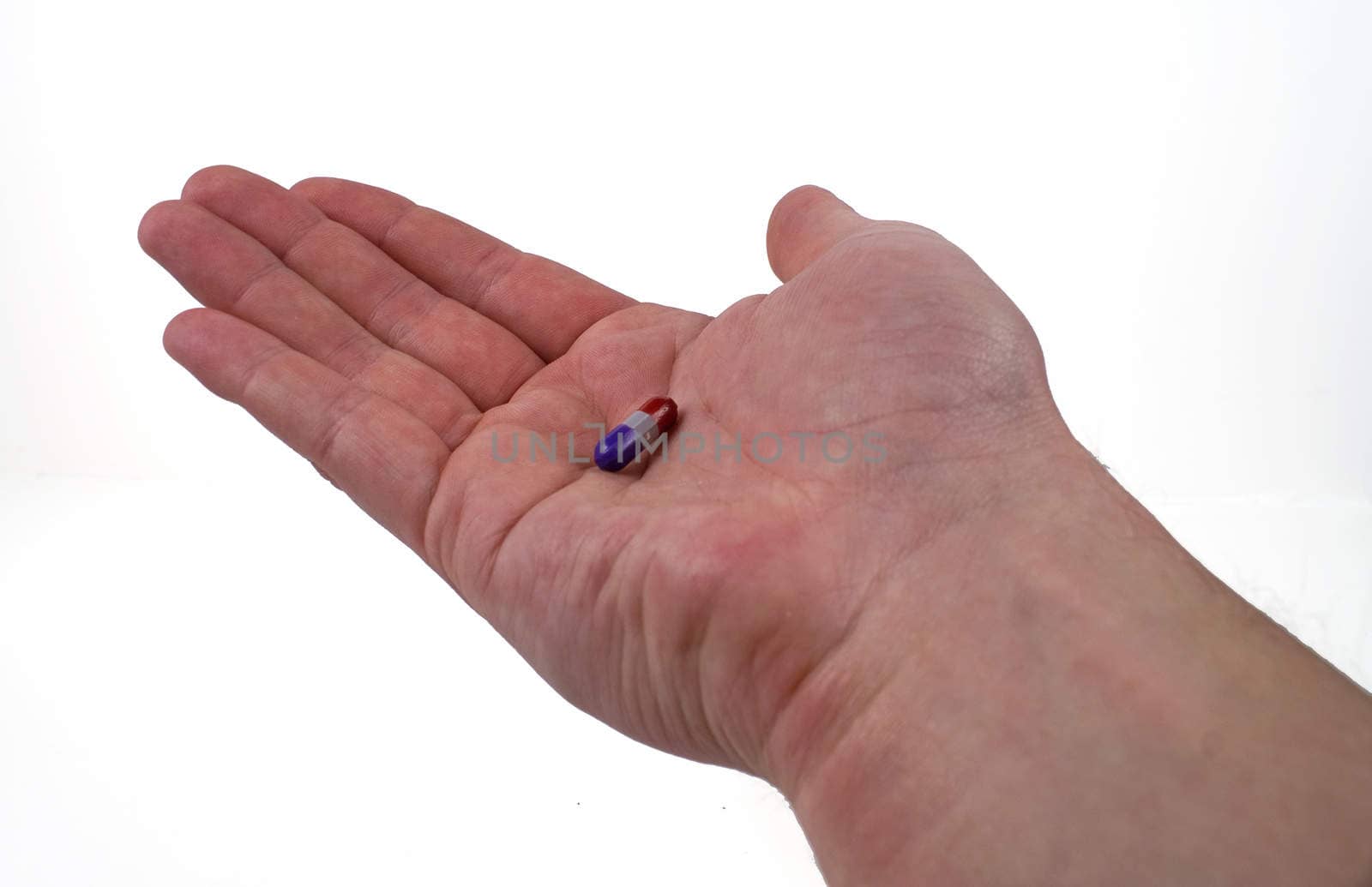 A single purple and red pill in the palm of a white man's hand against a white background.