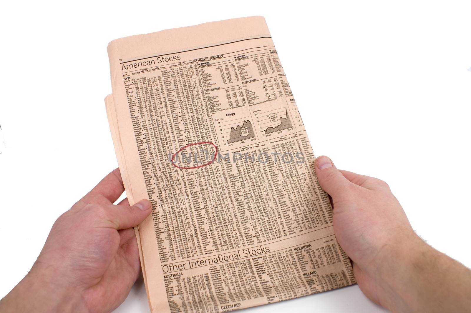 Male hands circle stock information in a newspaper against a white background.
