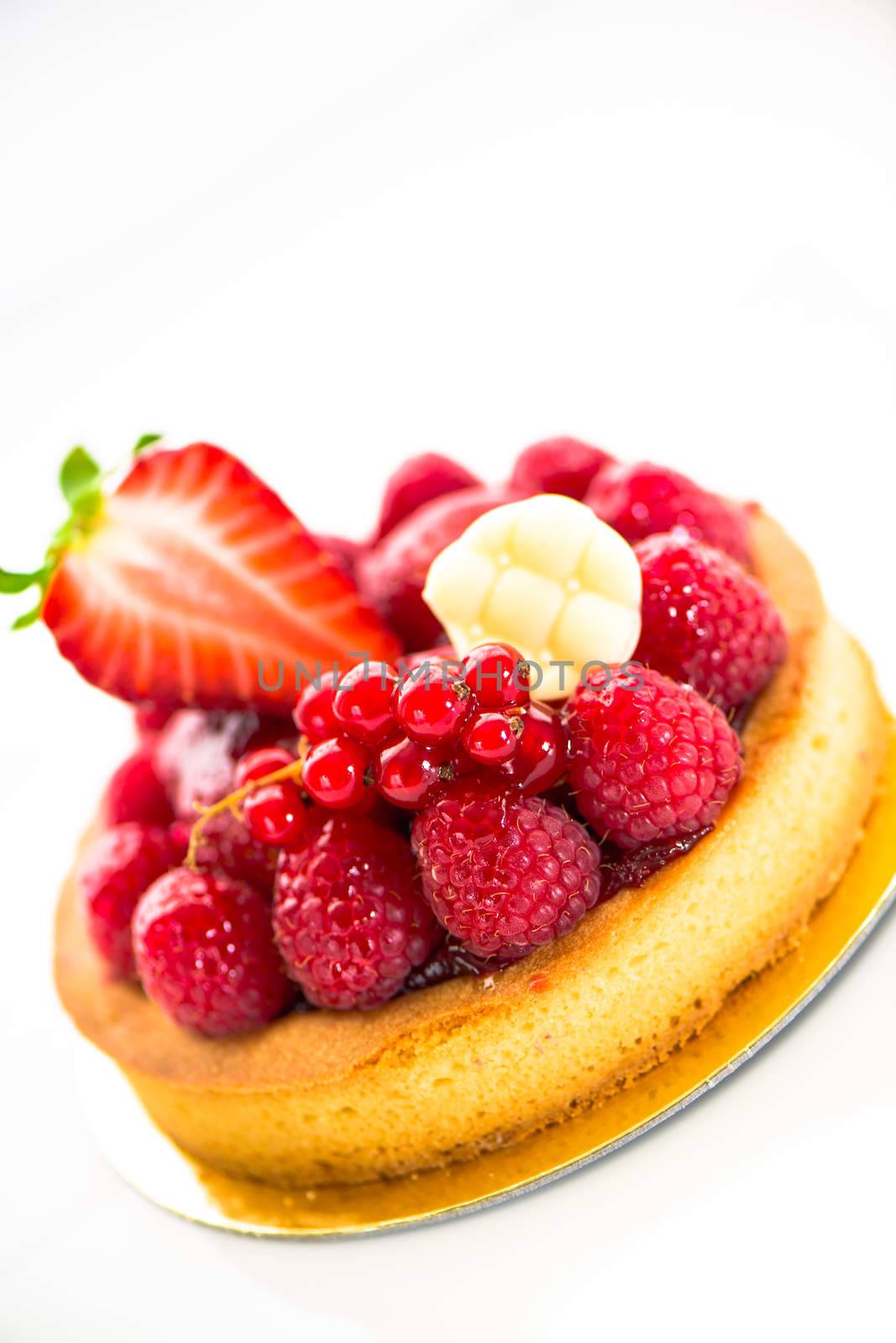 A small fruits tart with strawberry raspberry currant and a piece of chocolate on white background