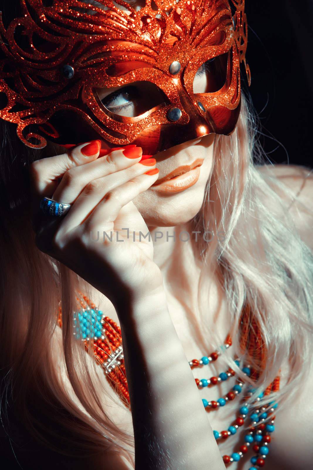 Blond lady in jewelry holding masquerade mask