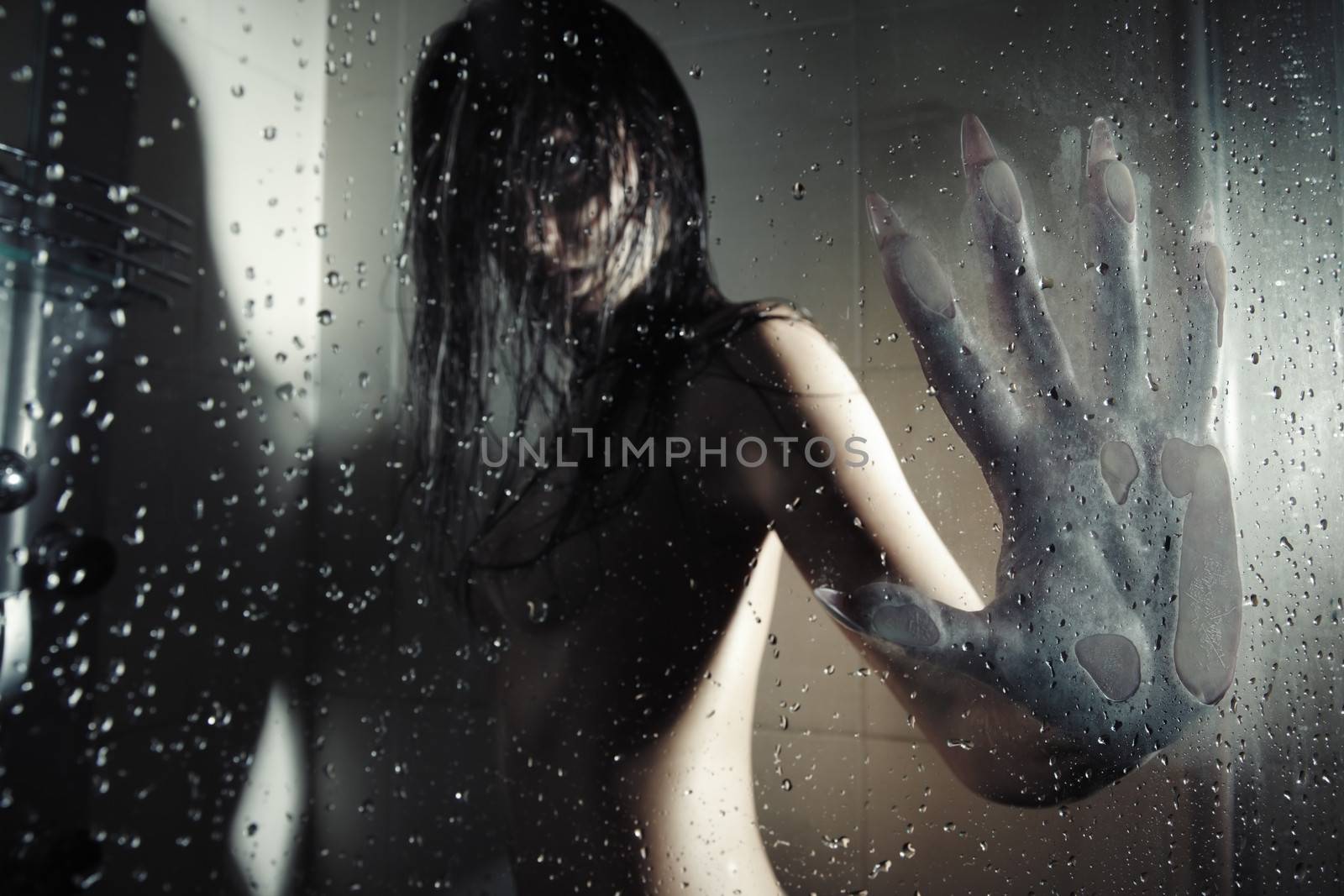 Female werewolf in the dark bathroom touching wet glass by his huge hand with sharp nails. Natural darkness. Artistic colors and grain added