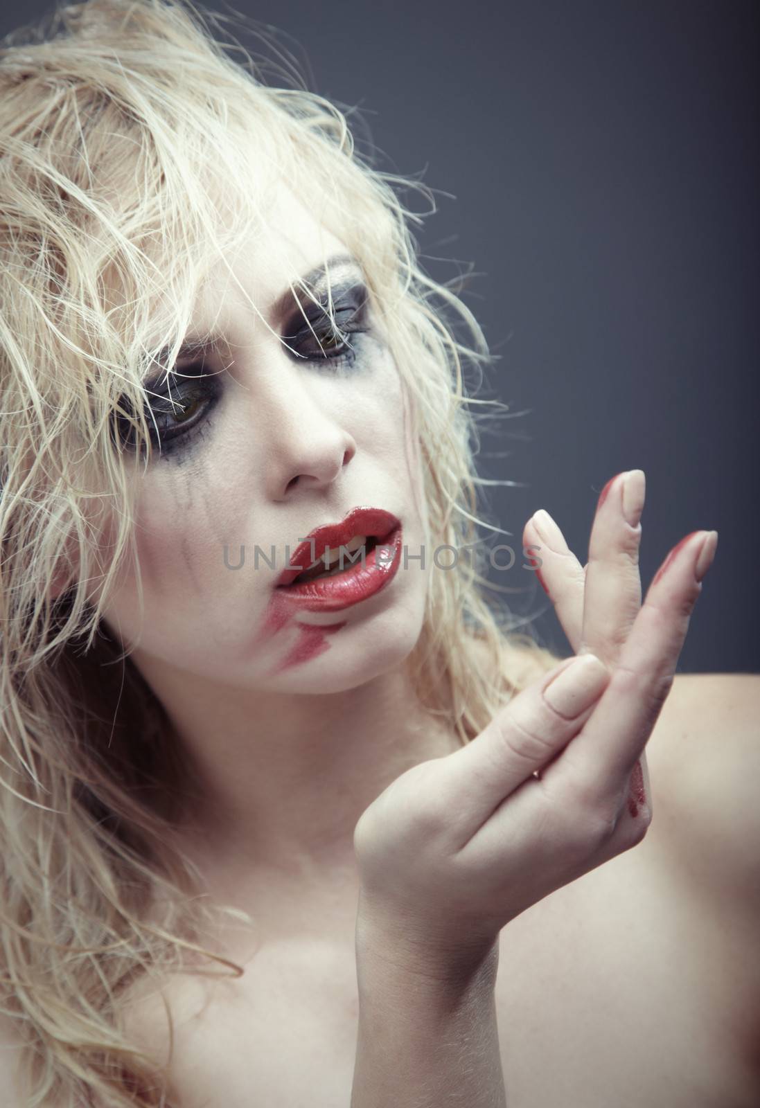 Crazy blond lady with bizarre dirty makeup on a dark background