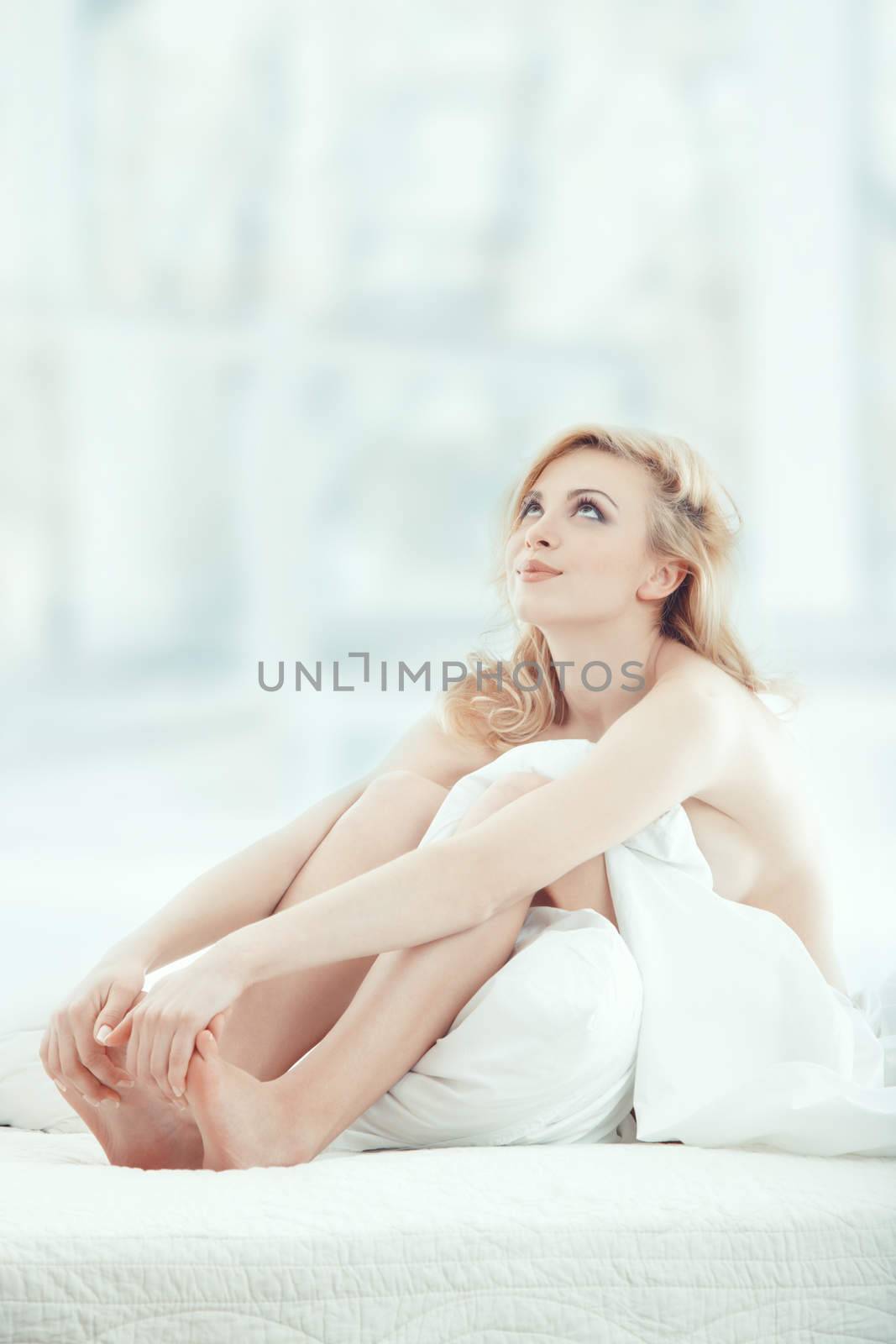 Attractive blond lady sitting on the bed at early morning