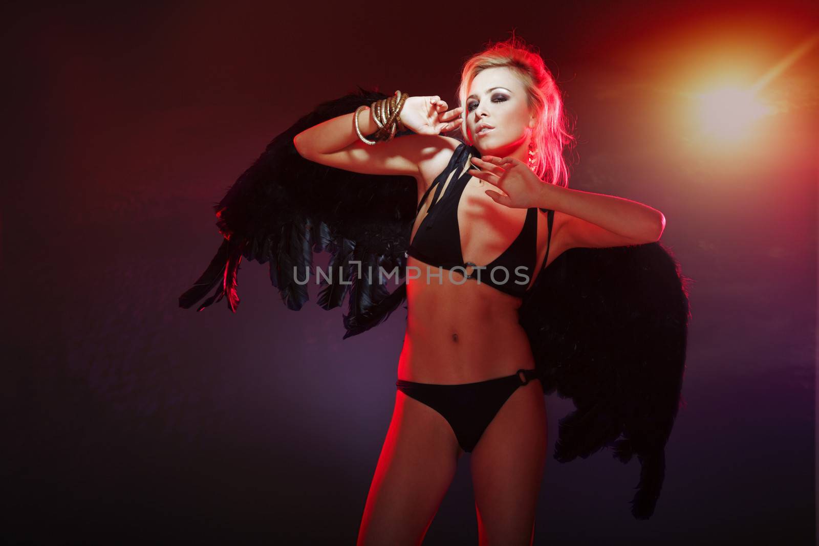 Woman in black lingerie with fallen angel wings standing against evening sky. Artistic colors and grain added