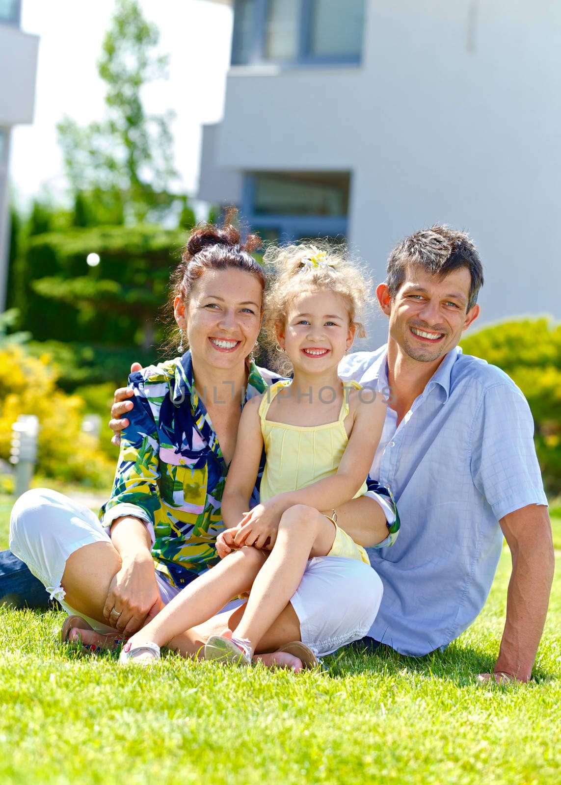 Happy family sitting on the lawn in front of his new cottage