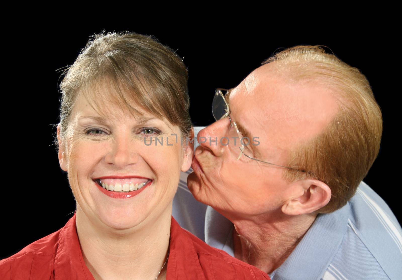 Middle aged husband gives his wife a peck on the ear.