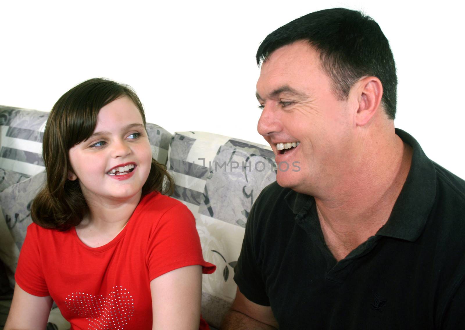 Father and his young daughter laugh together sitting on a sofa.