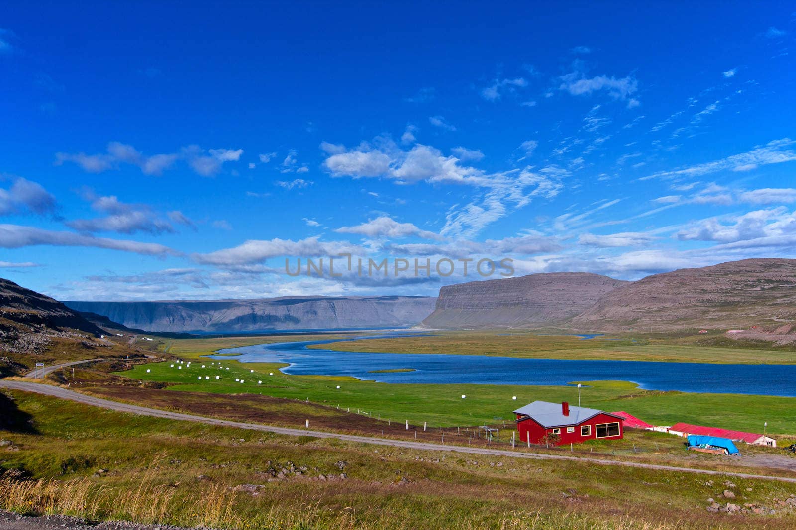 Beautiful red house in Iceland. Mountains, fjord, hay bales on the meadow in background.