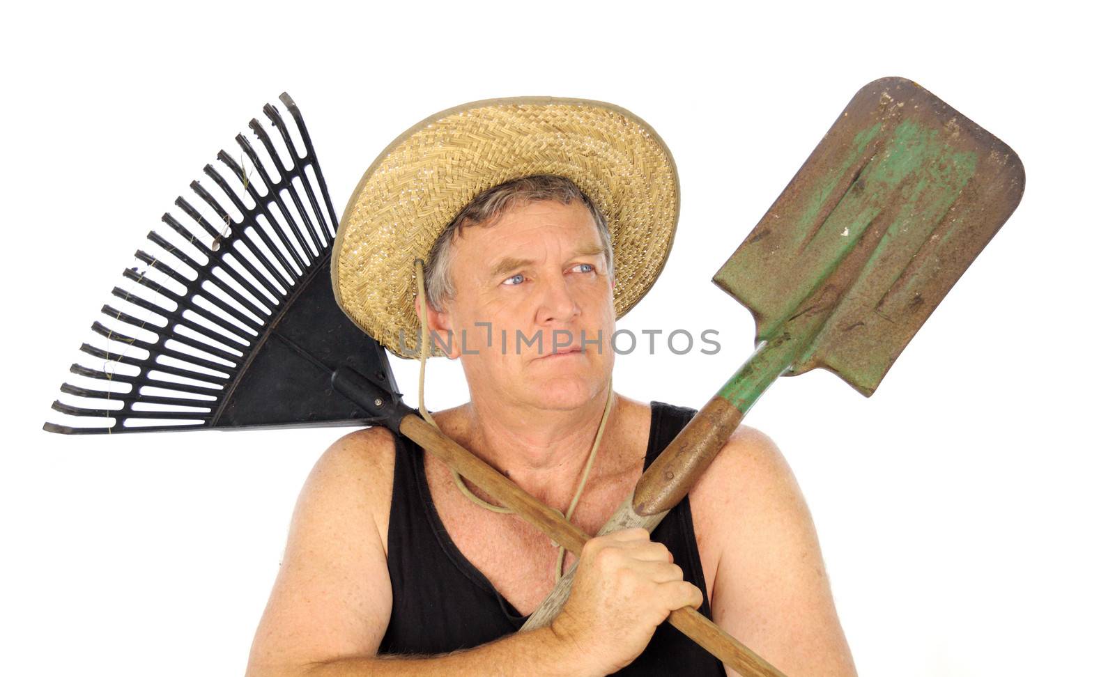 Serious middle aged gardener with straw hat holds a rake and spade.