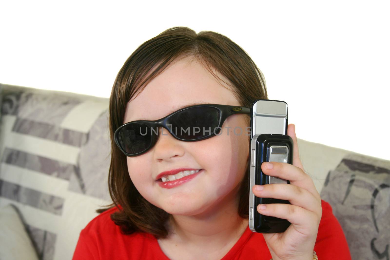 Little girl with sunglasses holds up her cell phone.