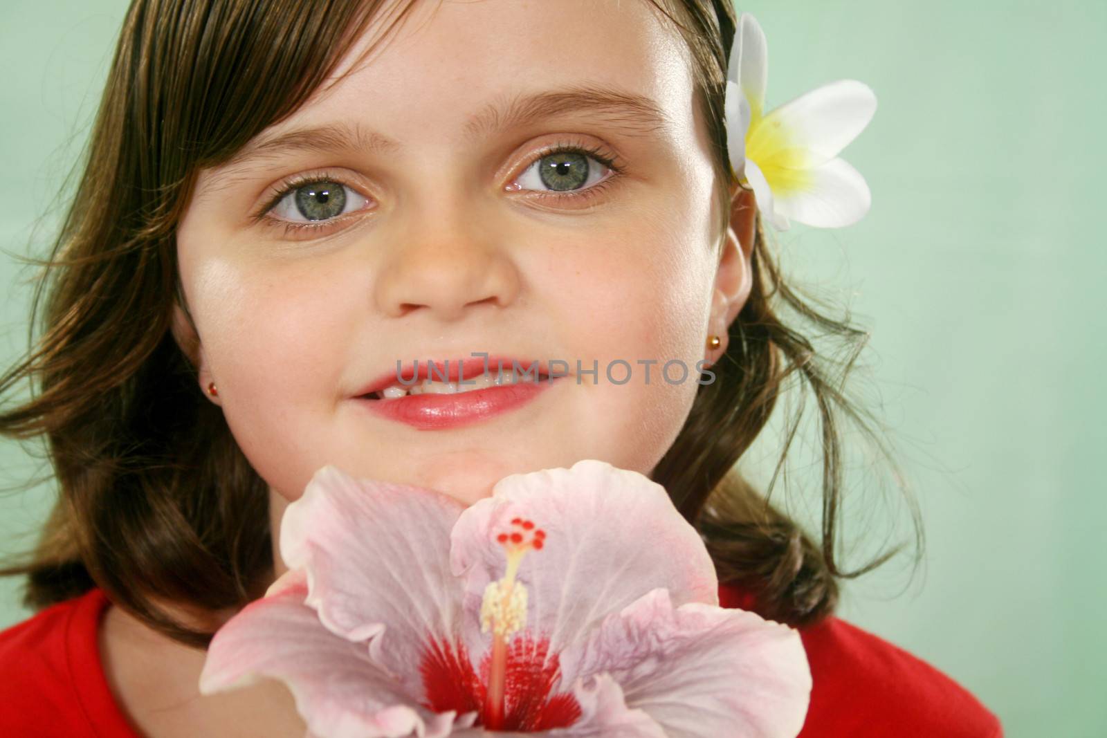 Little girl holding an hibiscus with a frangipani in her hair.