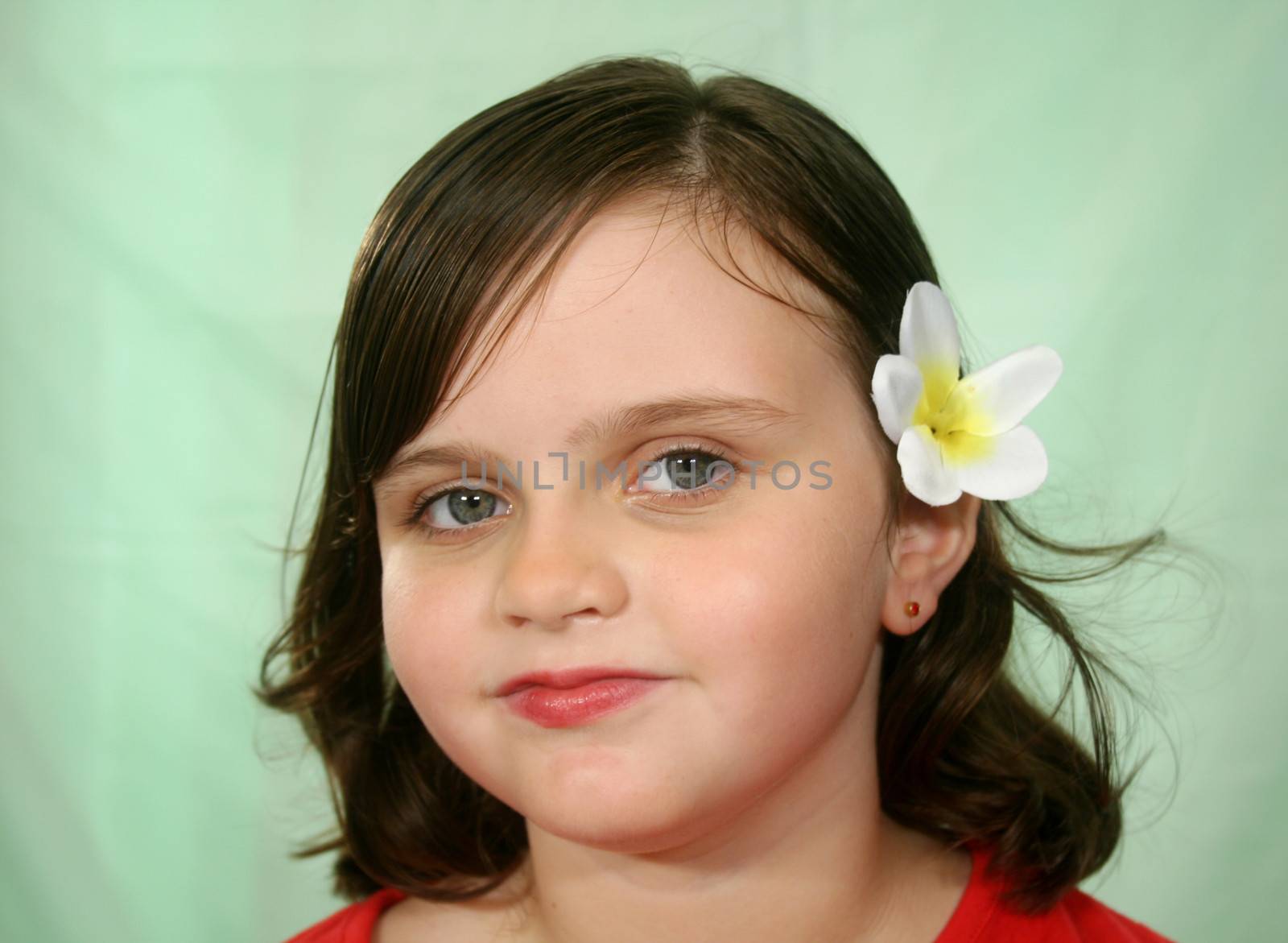 Little girl with frangipani flower in her hair looking at camera.