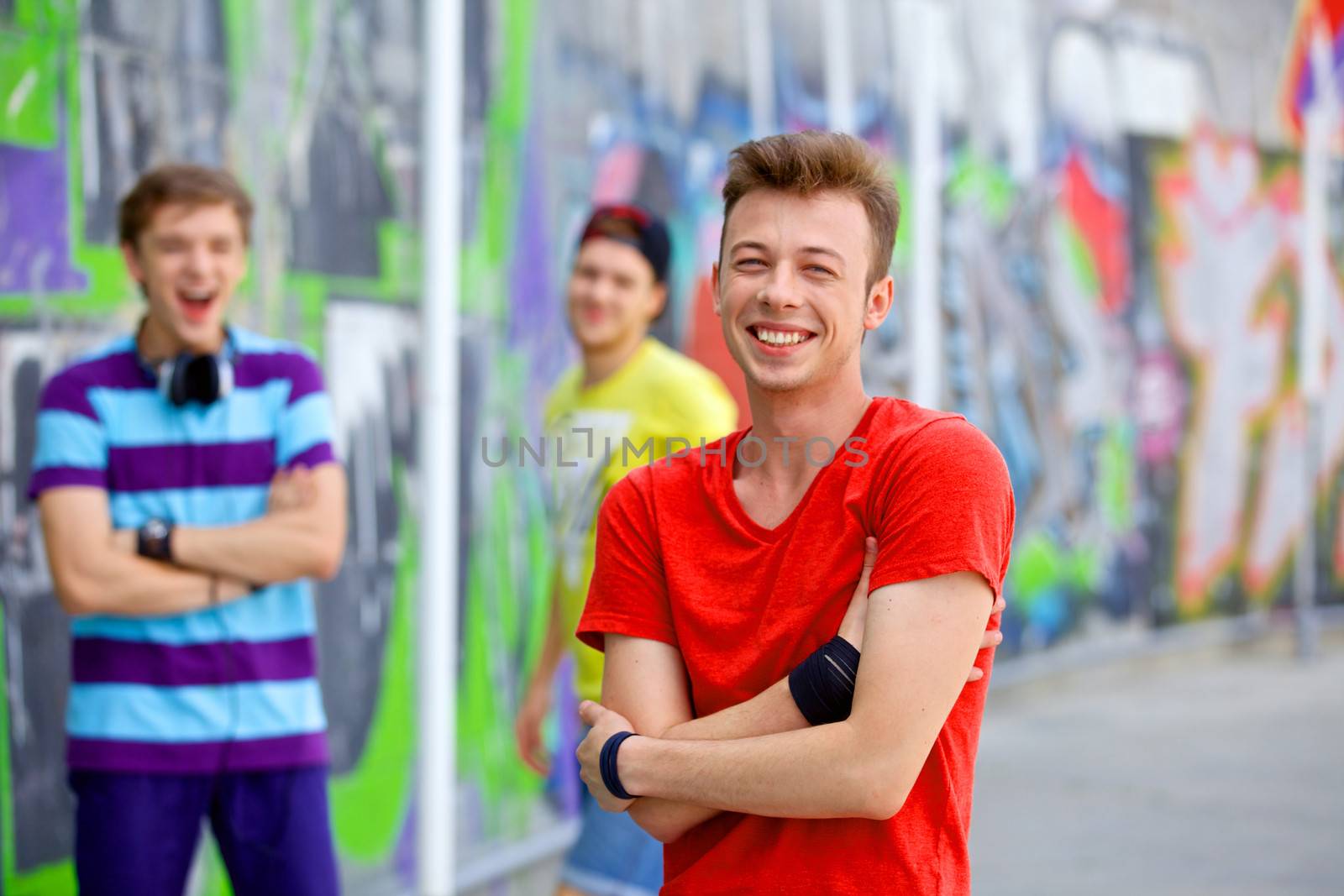 Portrait of happy teens boy with his friends by painted wall looking at camera