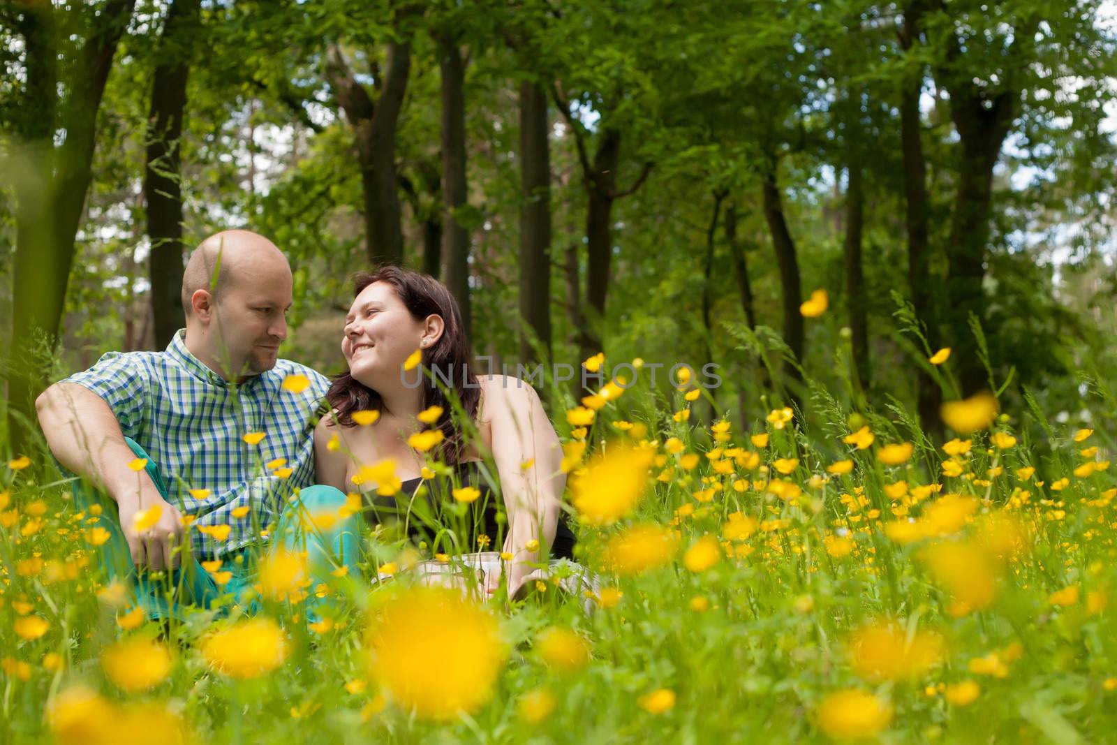 Happy young couple is sitting in a field of buttercups