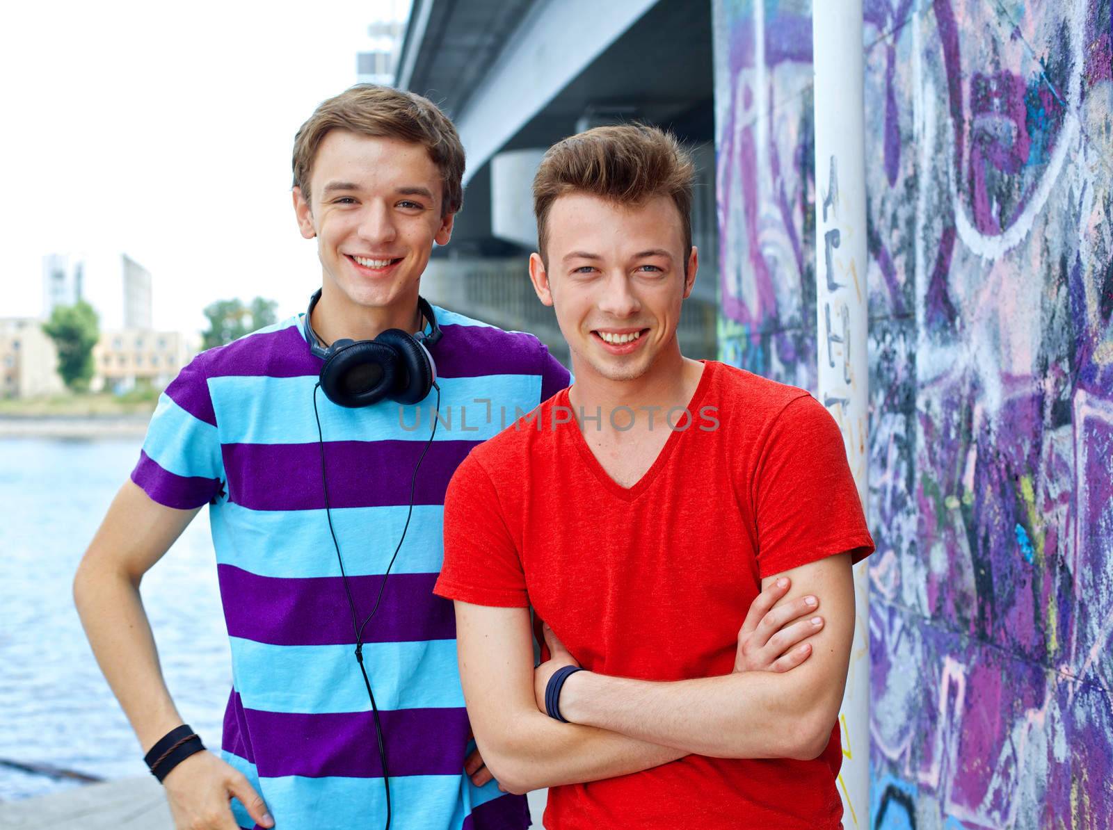 Portrait of happy two teens boys by painted wall looking at camera
