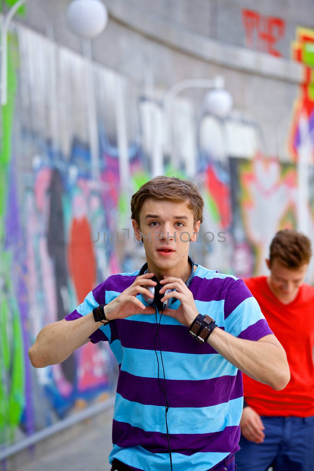 Portrait of happy teens boy with his friends by painted wall looking at camera. Vertical view