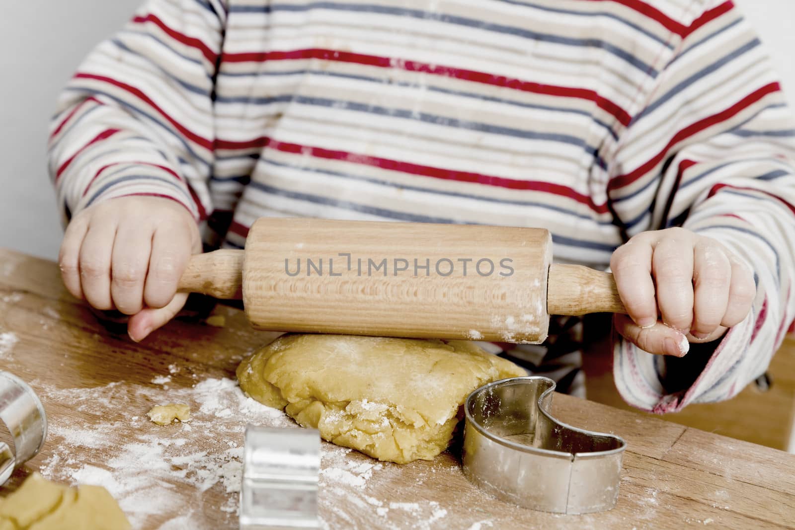 child rolling dough on wooden desk by gewoldi