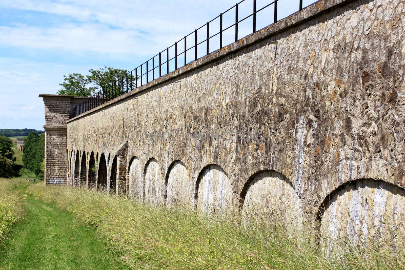 a former medieval bridge in a field on blue sky background