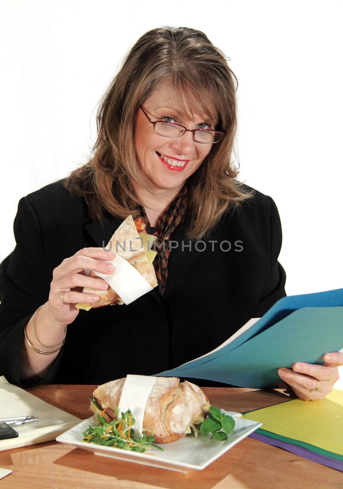 Middle aged businesswoman eats lunch while still working at her desk.